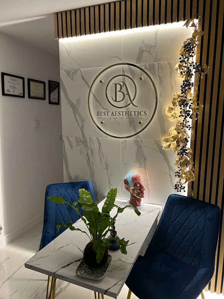 Consultation area at Best Aesthetics: marble table, blue chairs, and branded wall sign